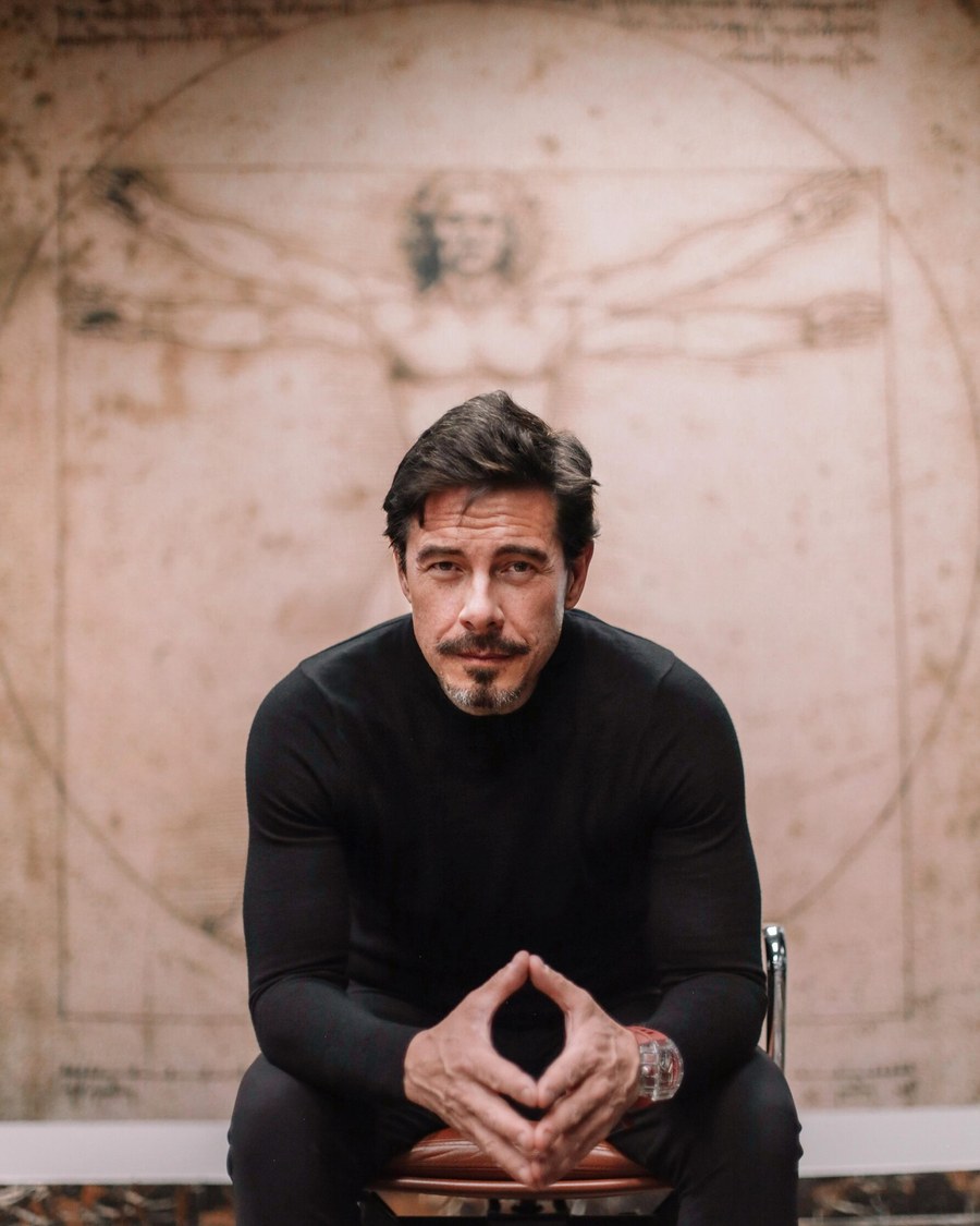 Robert Edward Grant seated in front of a large reproduction of Leonardo's Vitruvian Man